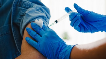 Healthcare professional giving flu antivirus vaccine injection to patient.  Healthcare provider is wearing blue gloves.