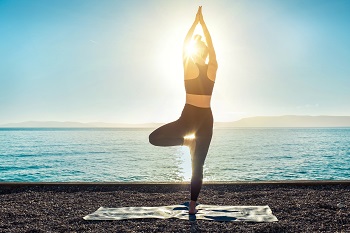 Image of Yoga Inspiration on nature.  A silhoutte of a woman in a yoga pose with the sunset and ocean behind her.