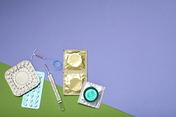 Contraceptive pills, condoms, intrauterine device and thermometer on color background, flat lay with space for text. Choice of birth control method